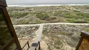 Eine Holztreppe führt zu einem Sandstrand mit Blick aufs Meer.