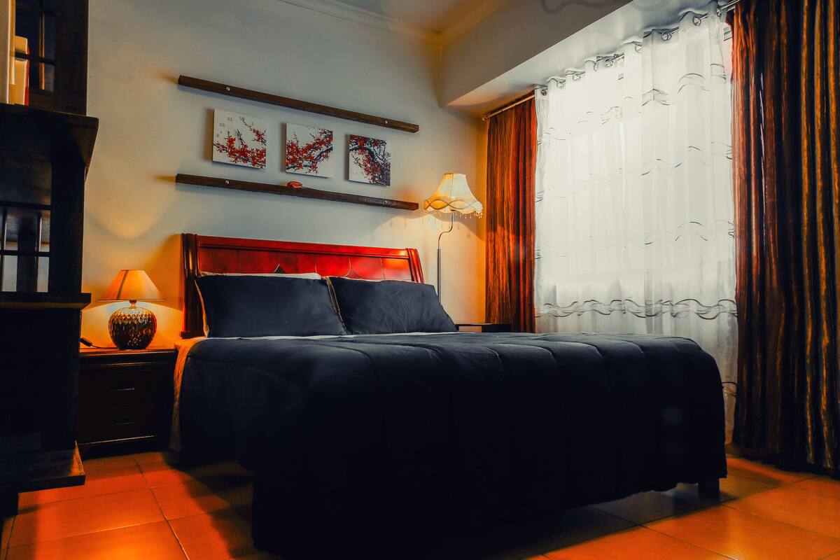 A neatly arranged bedroom with a bed, bedside lamps, and artwork on the wall.