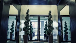 A modern hotel entrance with glass doors, potted evergreen trees, and a clean, tiled floor. - West Insula Units By AYS (Quezon City)