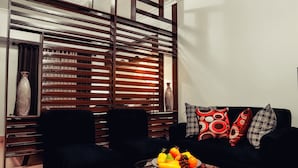 A modern living room with a black sofa, two black armchairs, a glass coffee table with fruit, and a wooden slatted partition. - West Insula Units By AYS (Quezon City)