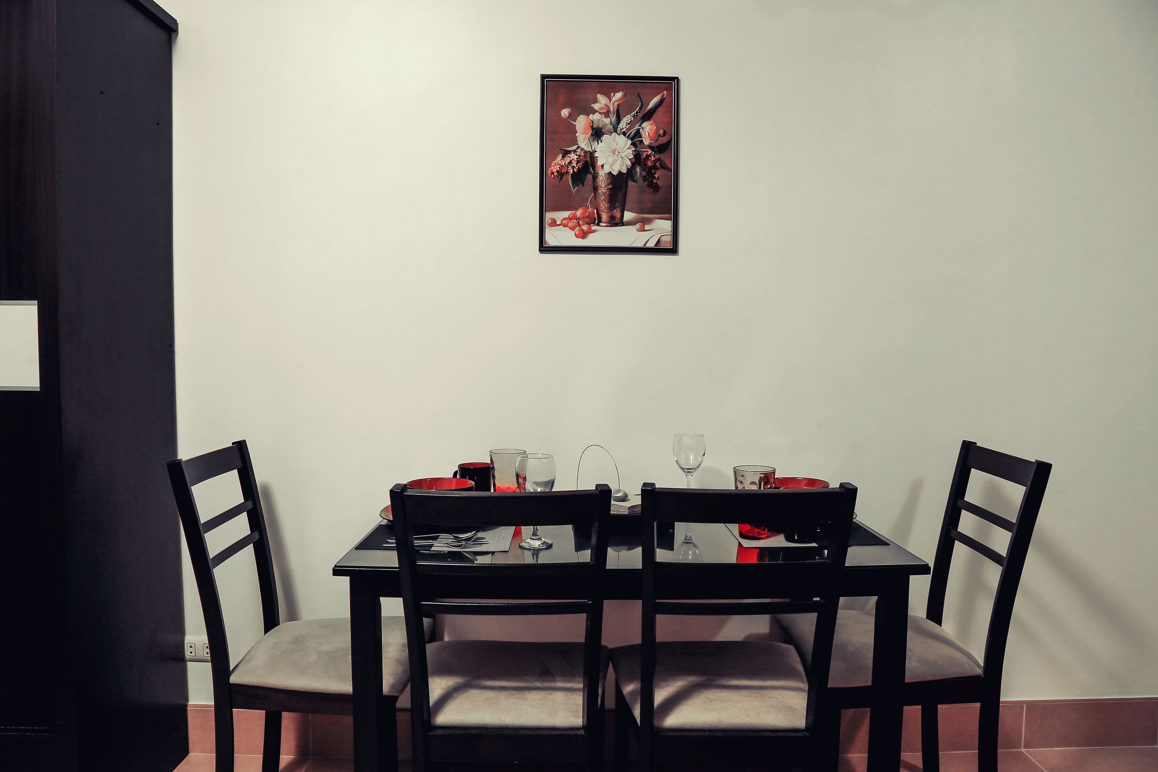 A dining table with four chairs, a framed artwork above, and a red bowl on the table.
