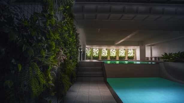 A modern indoor swimming pool with a greenish water feature, surrounded by a tiled floor and a vertical garden wall. - West Insula Units By AYS (Quezon City)