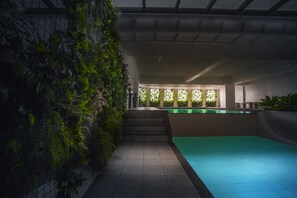 A modern indoor swimming pool with a greenish water feature, surrounded by a tiled floor and a vertical garden wall. - West Insula Units By AYS (Quezon City)