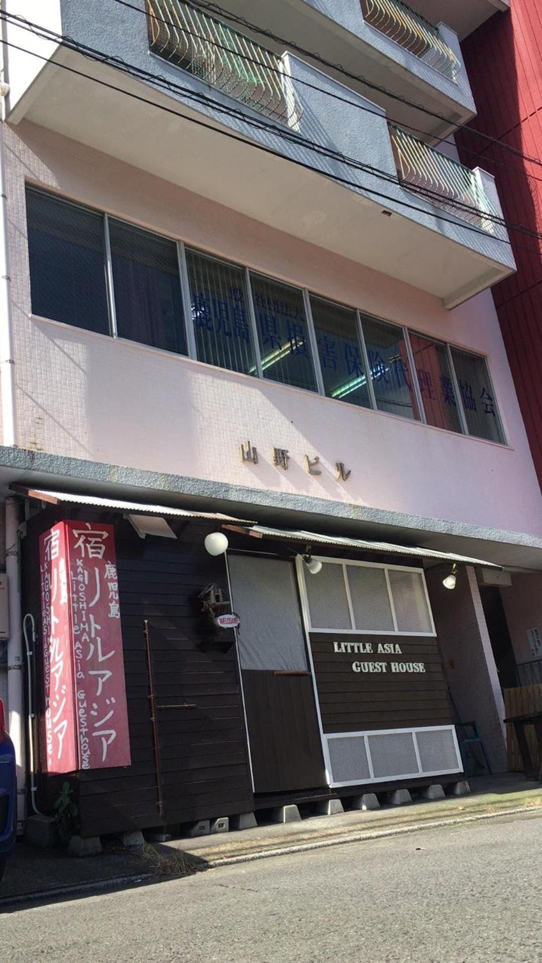 A building with a sign for 'Little Asia Guest House' and a red banner with Japanese text.