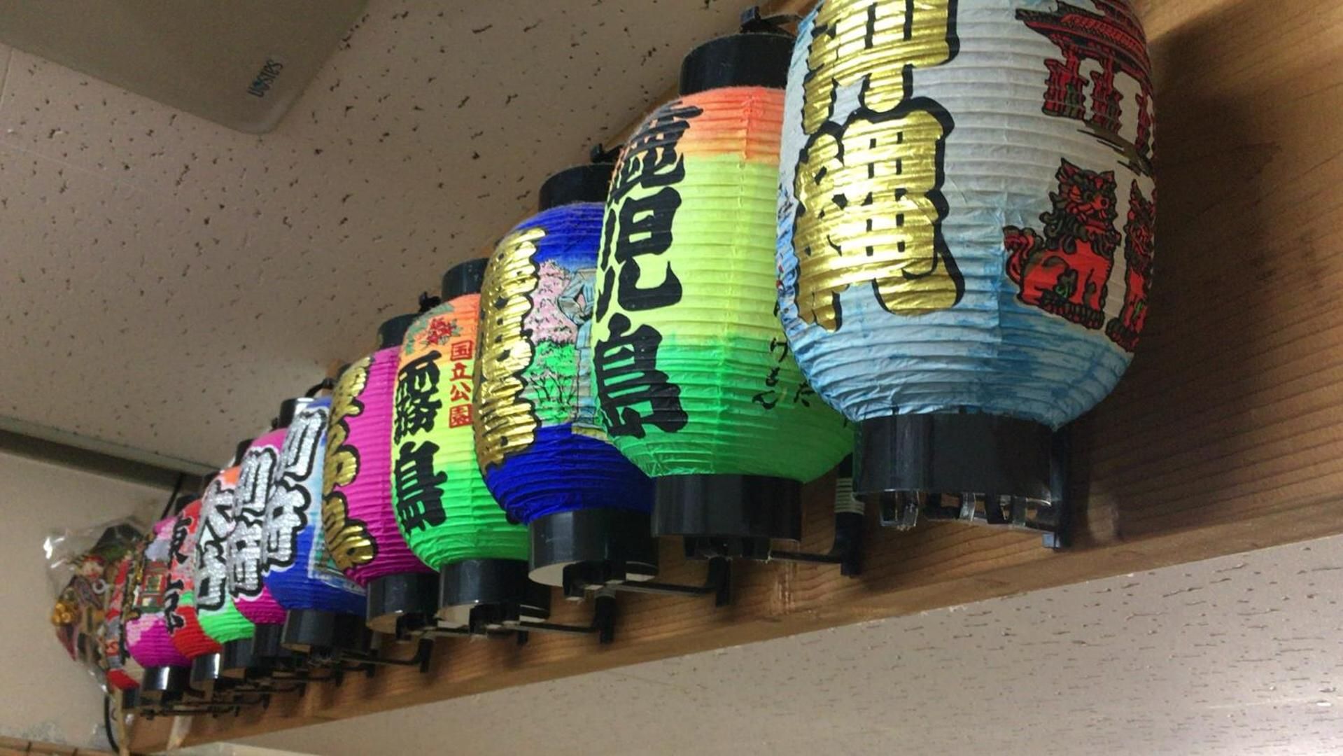 Une rangée de lanternes en papier aux couleurs vives, ornées de caractères japonais, est posée sur une étagère.