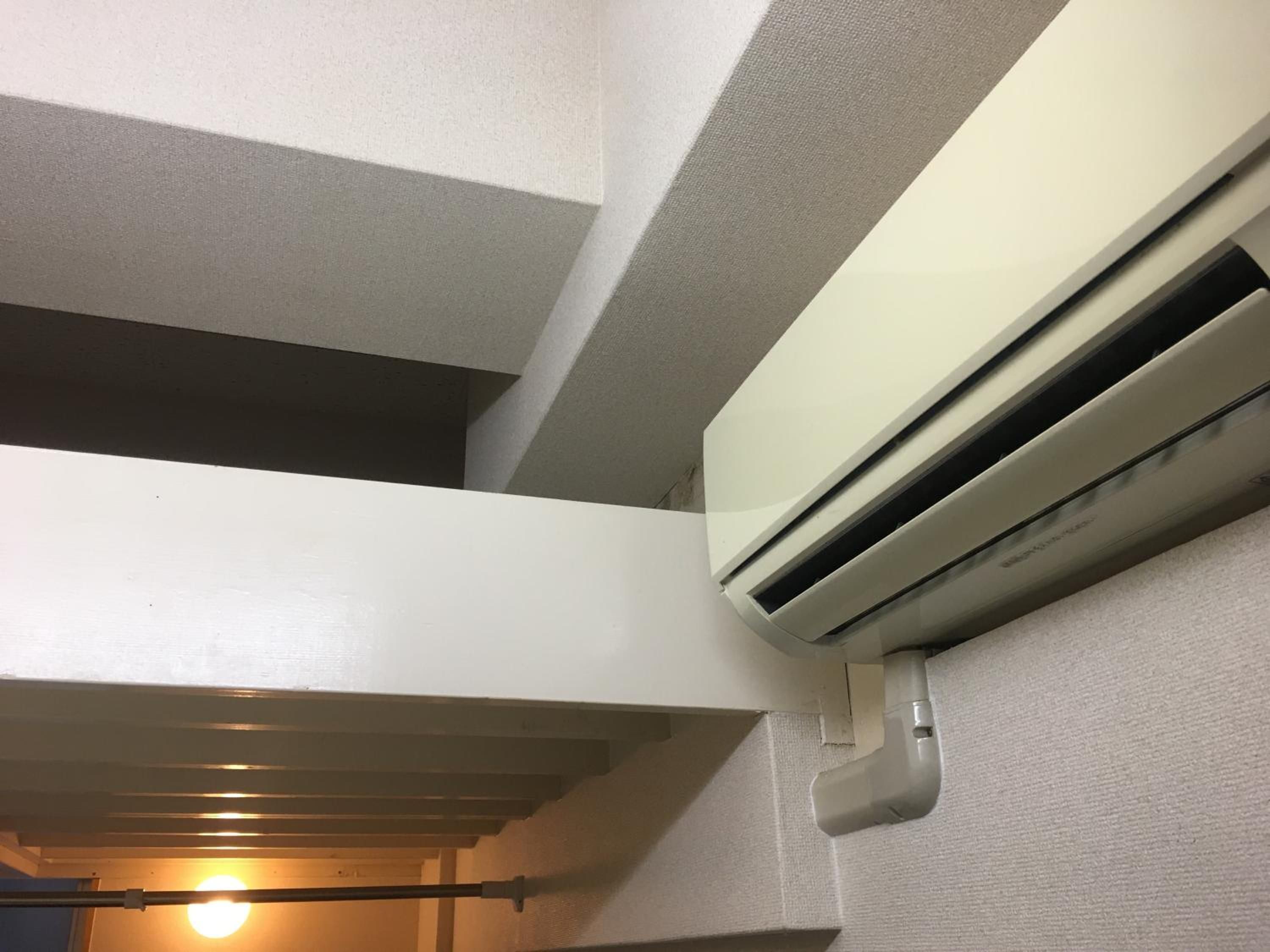 A white air conditioning unit mounted on a textured wall, with a ceiling fan and a light fixture visible in the background.
