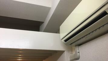A white air conditioning unit mounted on a textured wall, with a ceiling fan and a light fixture visible in the background.
