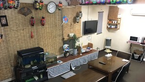 A room with a wooden table, benches, a fish tank, a clock, and various wall decorations including lanterns and a TV. - Kagoshima Little Asia - Hostel (Kagoshima)
