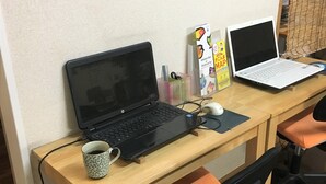 A wooden desk with two laptops, a mouse, and a mug. - Kagoshima Little Asia - Hostel (Kagoshima)