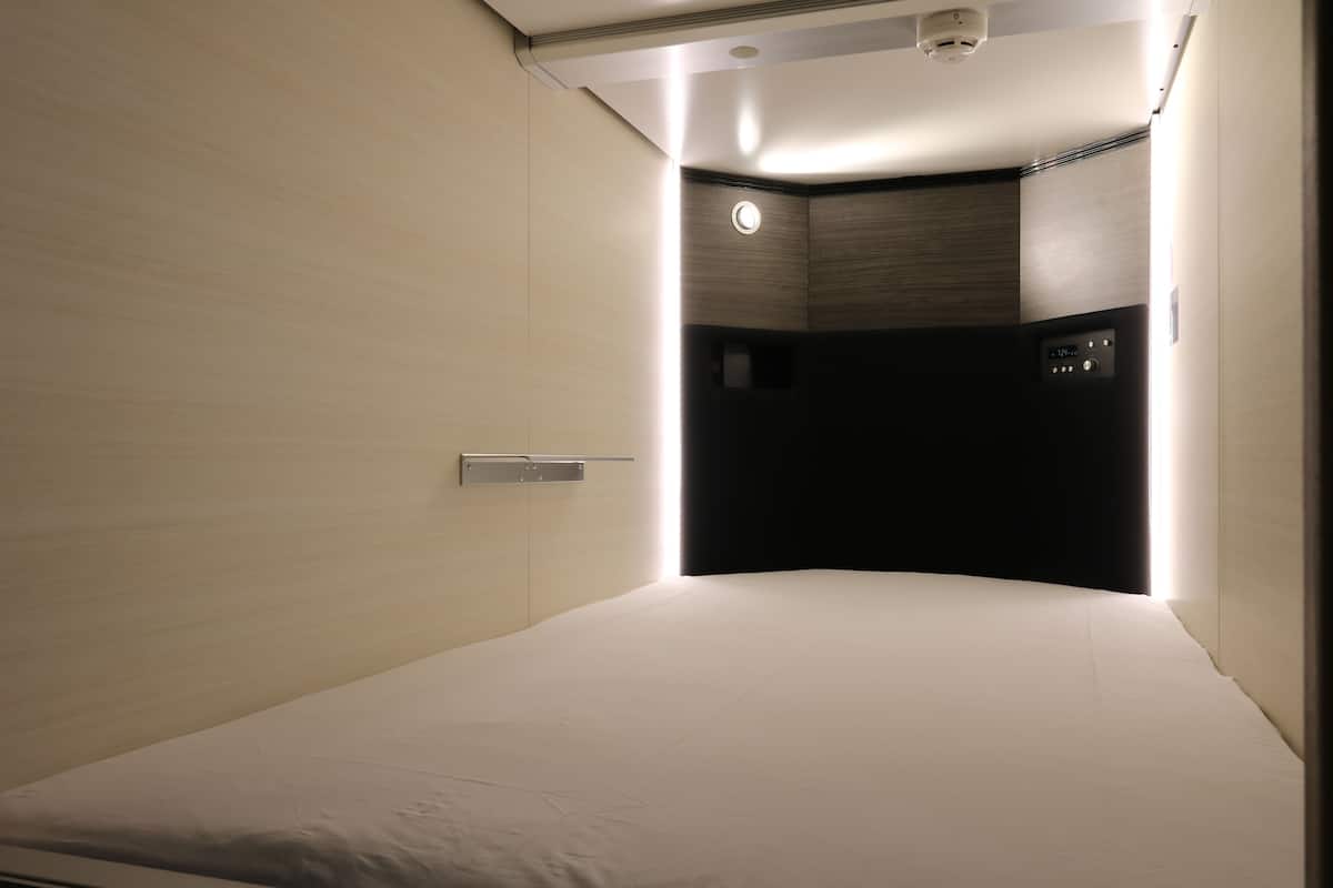 A modern hotel room with a curved bed, a control panel, and a small window.
