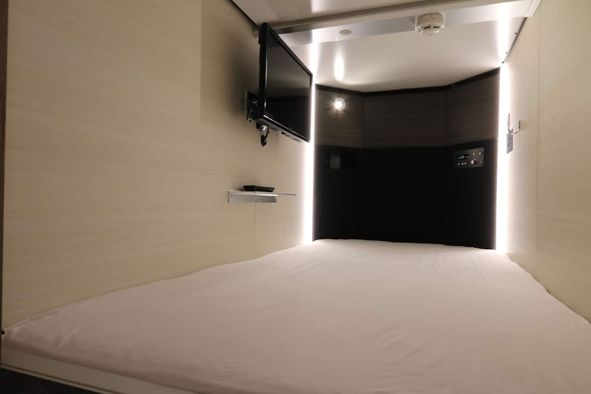 A hotel room with a bed, a mounted TV, and a control panel on the wall.