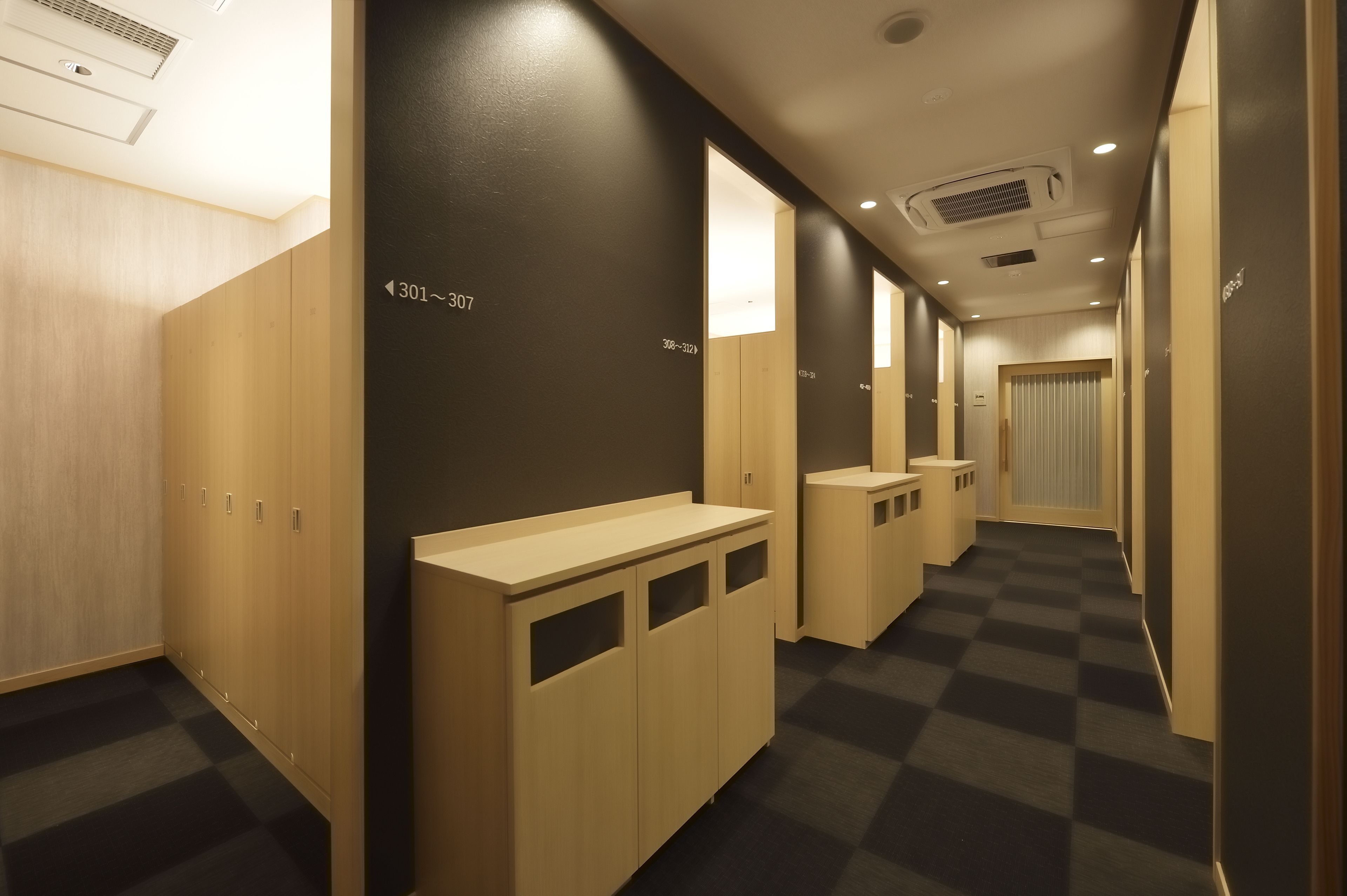 A hotel hallway with lockers numbered 301-307, a checkered floor, and a door at the end.