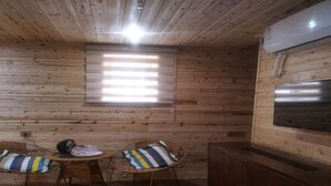 A cozy room with wooden walls, a small table with chairs, a ceiling fan, and a built-in air conditioning unit. - Nanjing Tulou Qingdelou Inn (Zhangzhou)