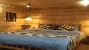 A wooden cabin room with a bed, a nightstand, a lamp, and a window with bars. - Nanjing Tulou Qingdelou Inn (Zhangzhou)