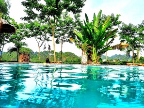 Ein klares Schwimmbecken, umgeben von üppiger Vegetation und einer Bergkulisse.