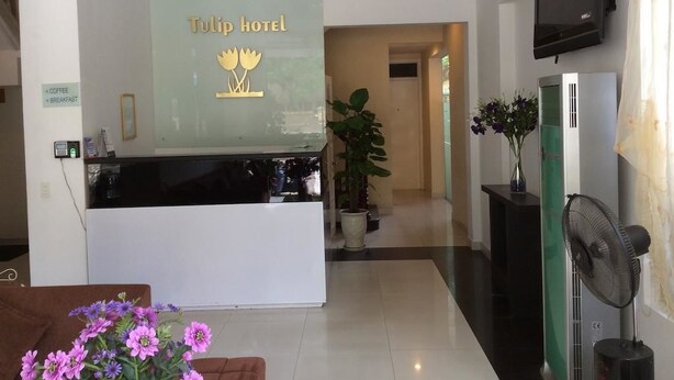 Un comptoir d’accueil avec une enseigne indiquant « Hôtel Tulip » et, à proximité, une autre enseigne indiquant « Café + Petit-déjeuner ».