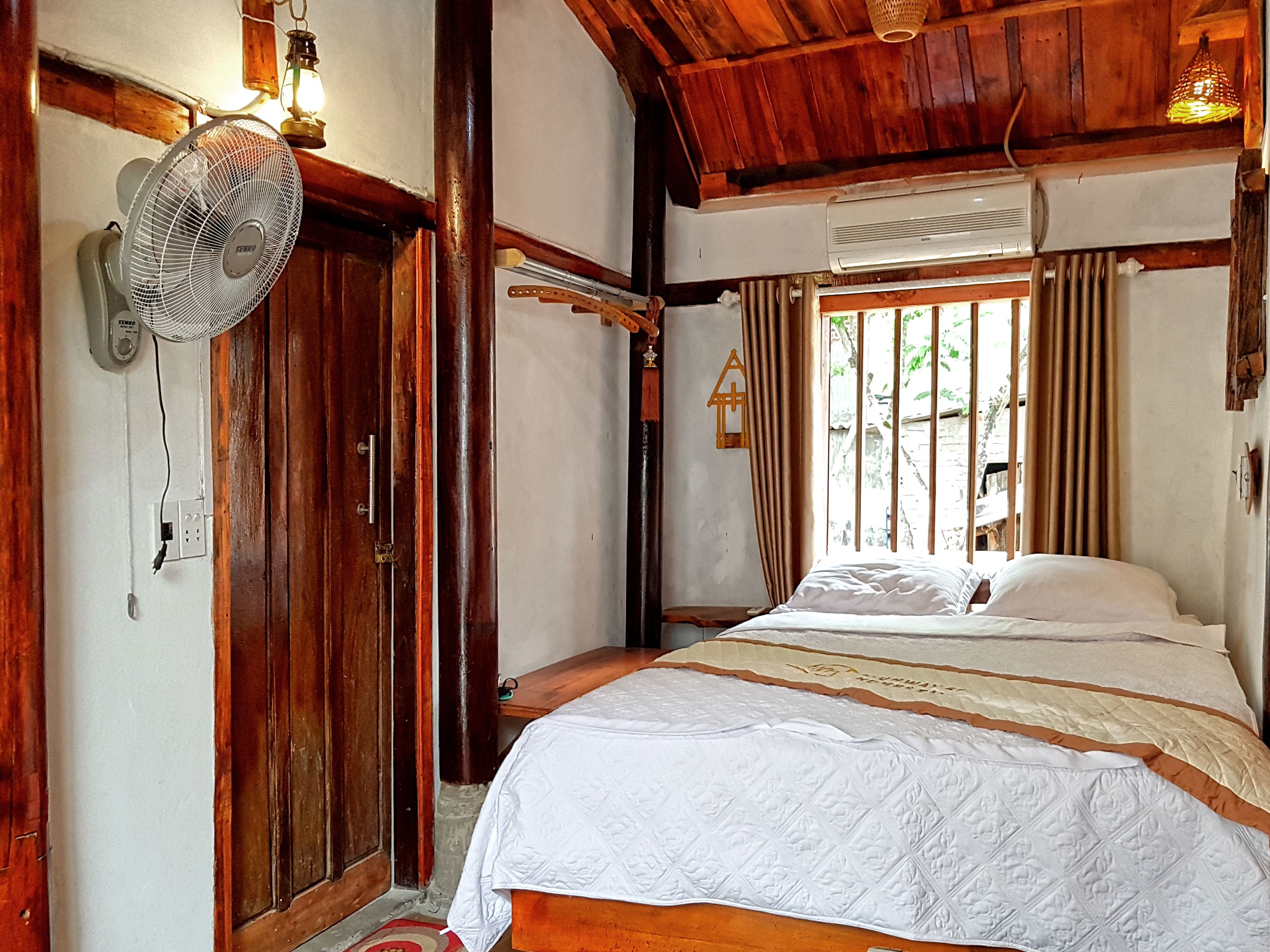 Una habitación de madera con una cama, un ventilador y una ventana con cortinas.