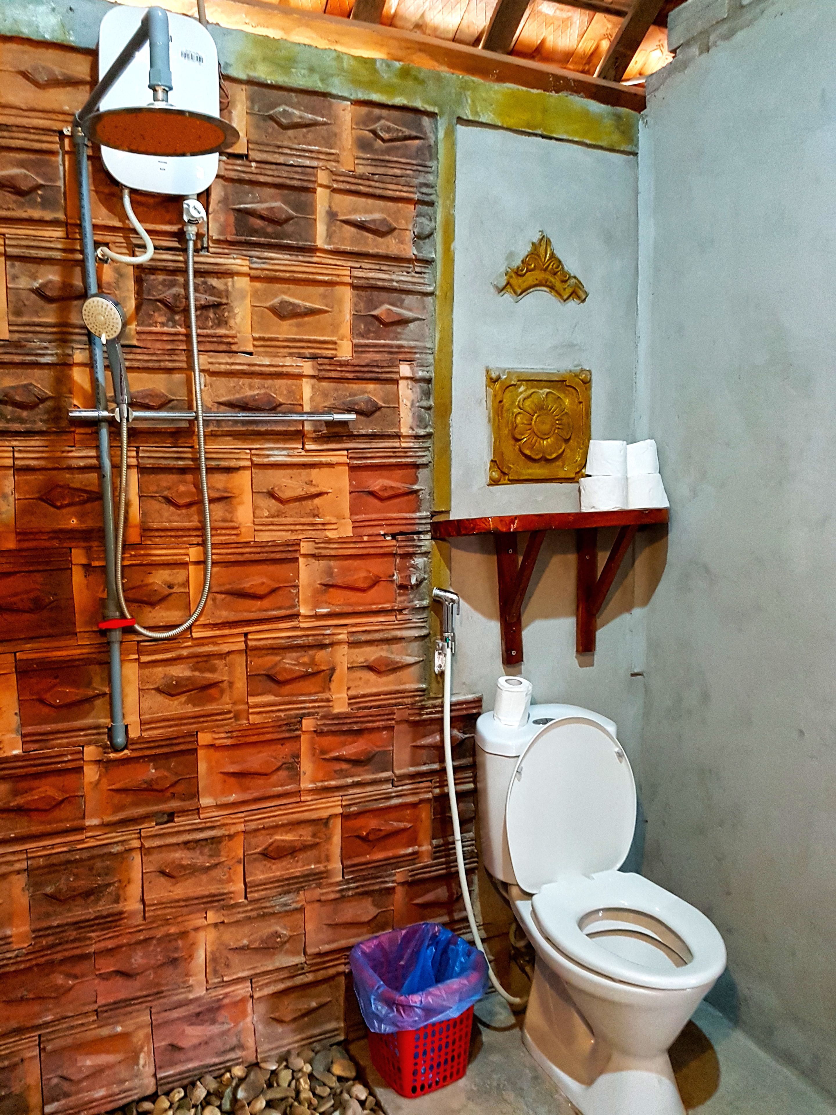 A bathroom with a wooden wall, a shower, a toilet, and a small shelf with toiletries.