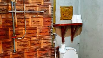 A bathroom with a wooden wall, a shower, a toilet, and a small shelf with toiletries.