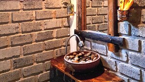 Uma casa de banho rústica com parede de pedra, um banco de madeira, uma tigela de fruta e um candeeiro suspenso.