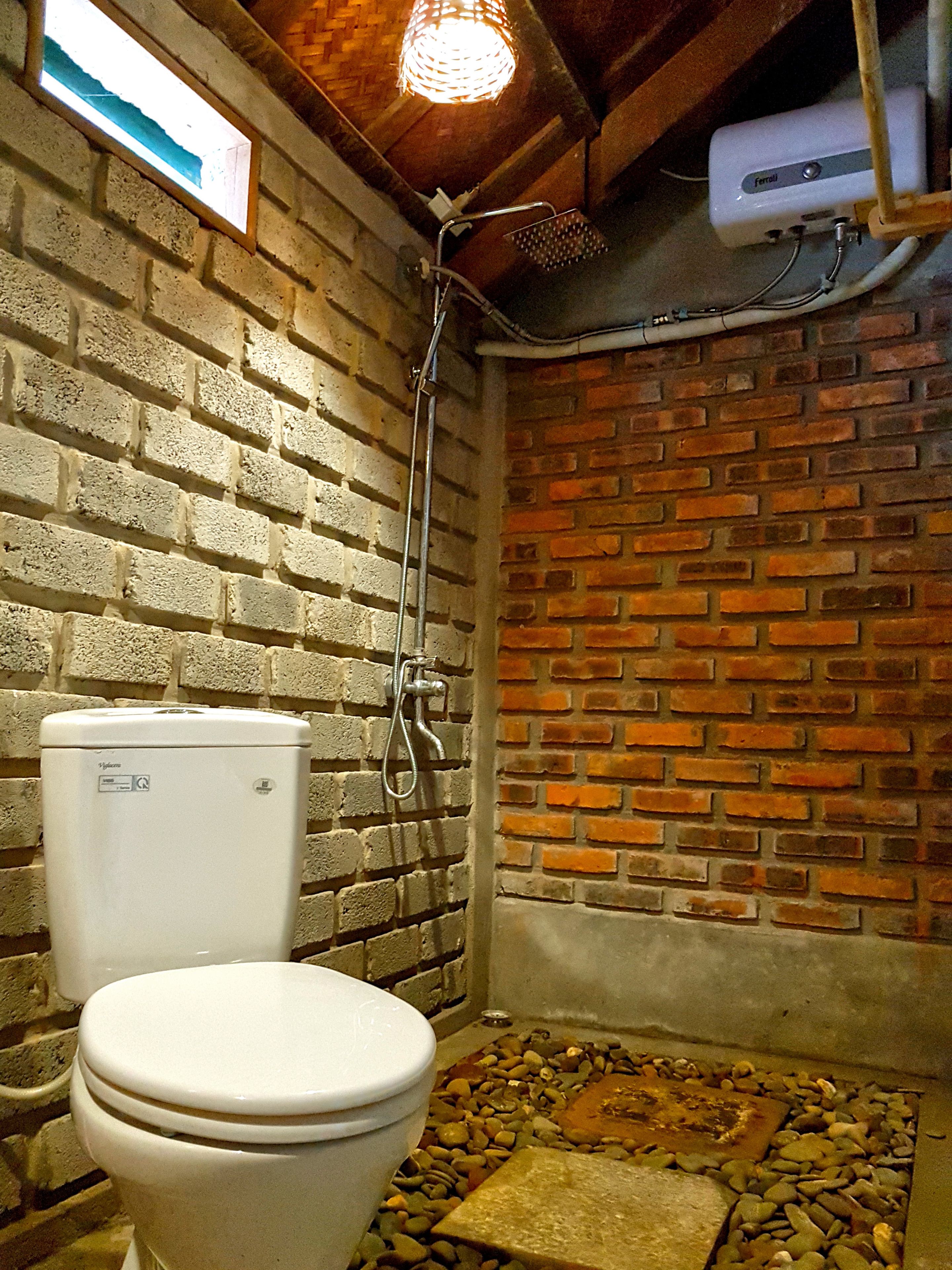 Un baño pequeño y rústico con inodoro blanco, ducha y pared de ladrillo.