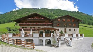 A traditional chalet with a wooden facade, multiple balconies with flower boxes, and a stone staircase leading to the entrance. - Hotel Rainhof (Senales)