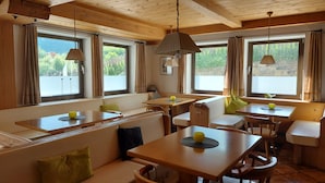 A cozy dining area with wooden tables and benches, large windows with curtains, and hanging pendant lights. - Hotel Rainhof (Senales)
