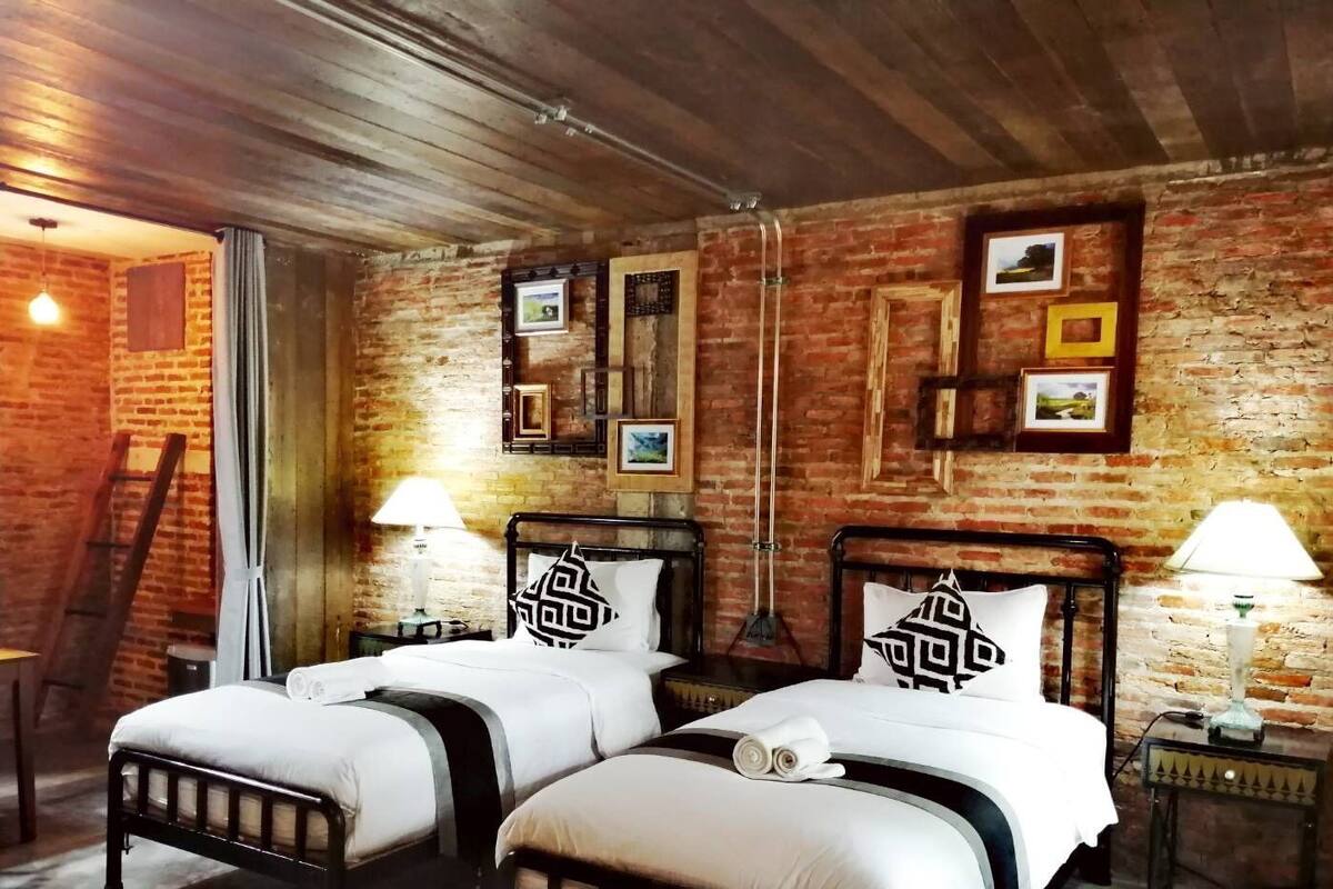 A room with two beds, a brick wall, and framed pictures.