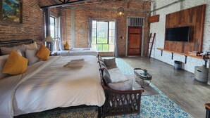 Una habitación con una cama grande, una silla de madera, un televisor montado en la pared y una ventana con cortinas.