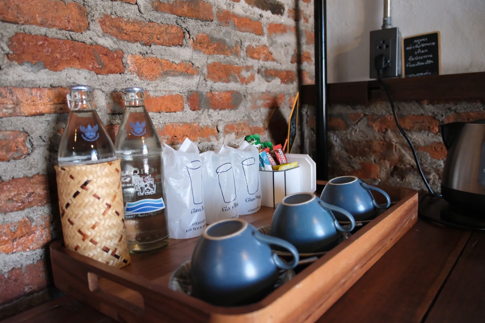 A tray with glassware and a bottle, a brick wall, and a coffee machine in the background.