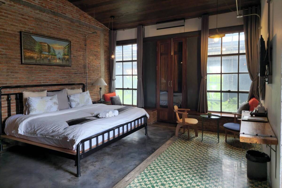 A bedroom with a brick wall, a bed, a desk, and a chair.