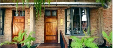 Un edificio rústico con dos puertas de madera, numeradas 2 y 3, y un ventanal con cortinas.