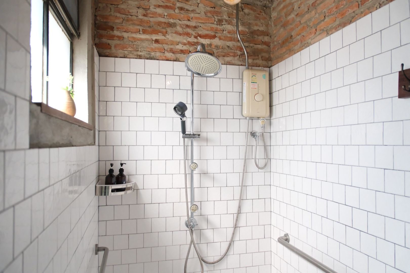 Un baño con paredes de azulejos blancos, una ducha con cabezal de ducha manual, otro cabezal de ducha manual, un cabezal de ducha empotrado en la pared y un panel de control.