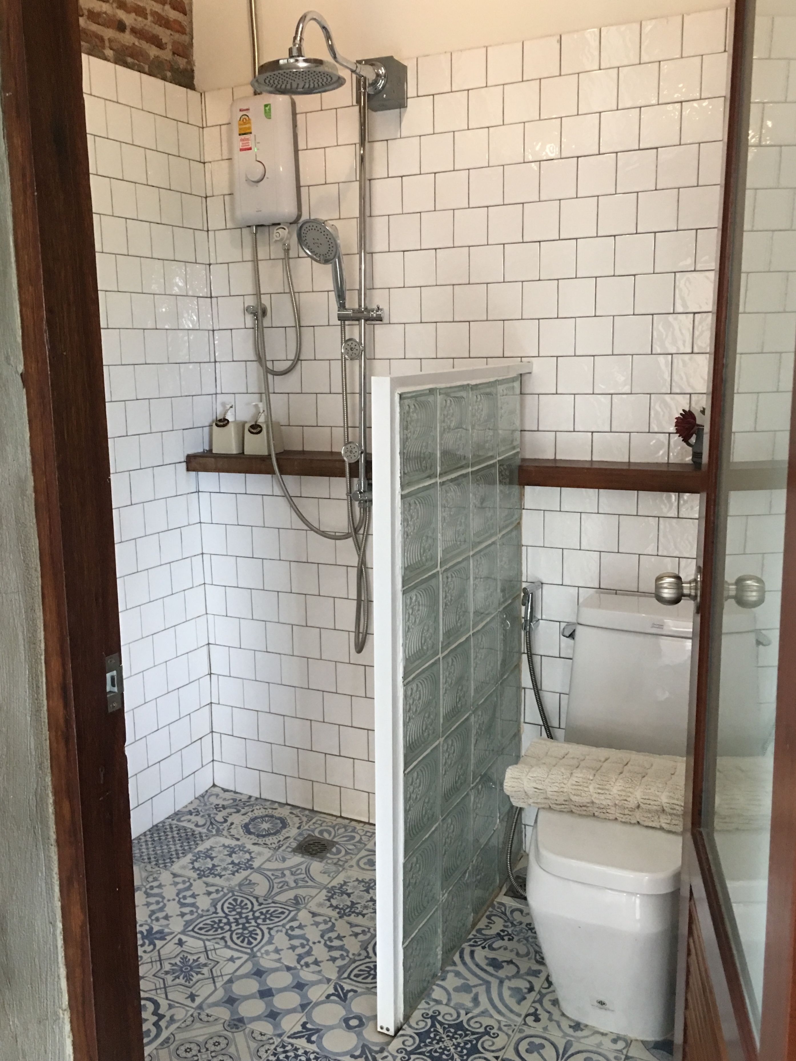 Un baño pequeño con paredes de azulejos blancos, una ducha, un inodoro y baldosas de suelo con diseño.