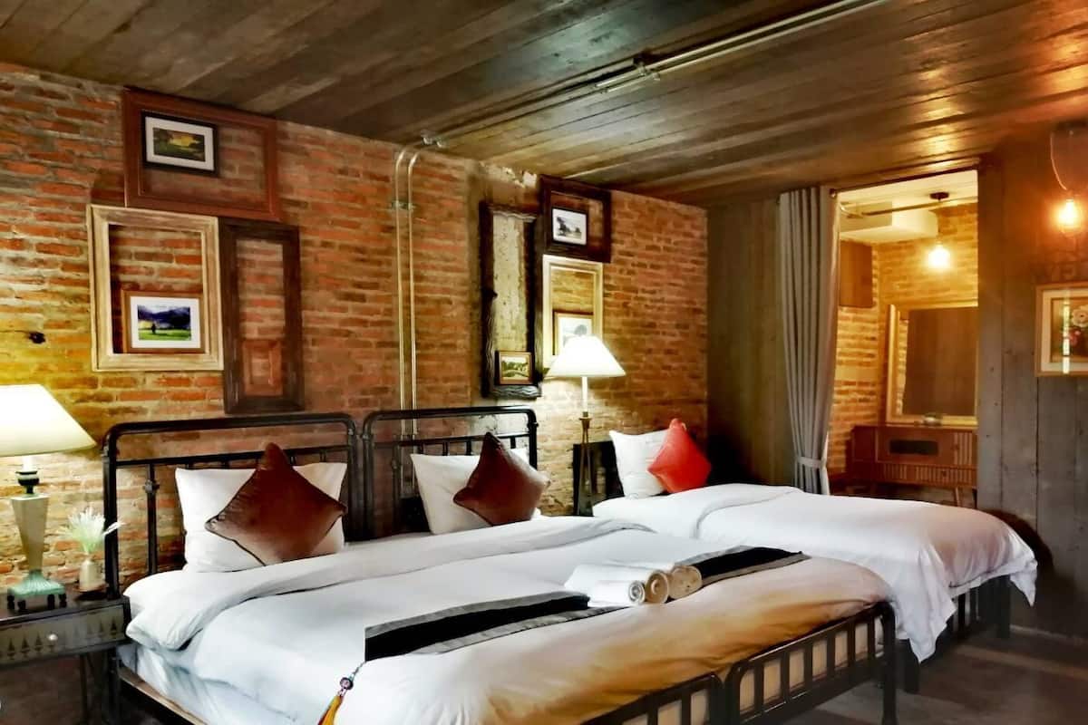 A double bed with a wooden headboard, a nightstand with a lamp, and a brick wall with framed pictures.