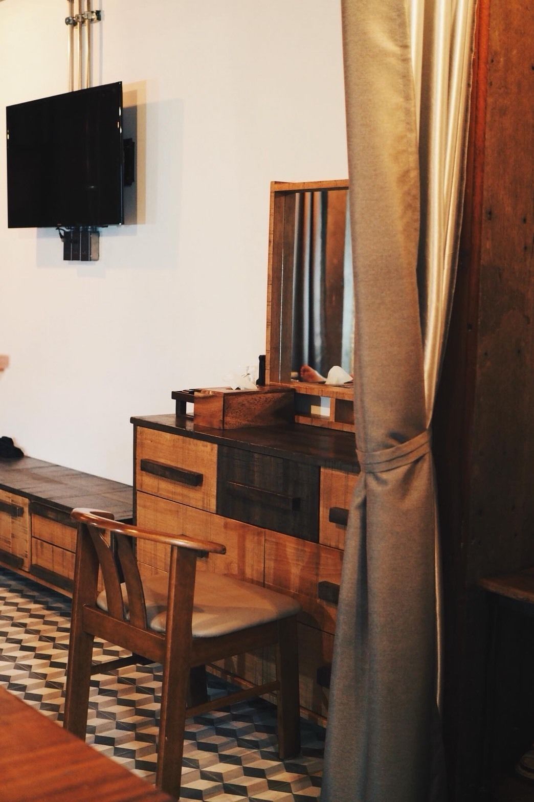A wooden dresser with drawers, a mirror, and a television mounted on the wall.