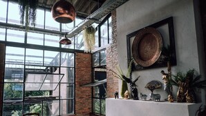 Una habitación con ventanas amplias, una pared de ladrillo y una estantería con objetos decorativos.