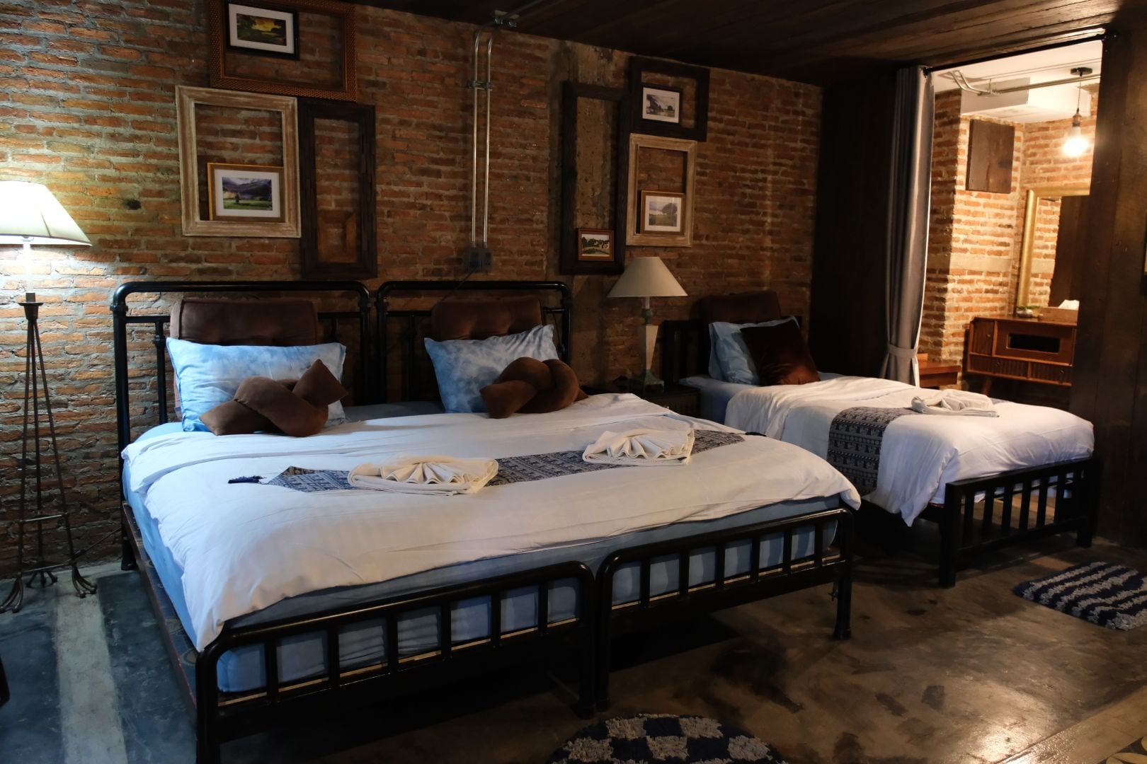 A hotel room with two beds, a brick wall, and framed pictures.