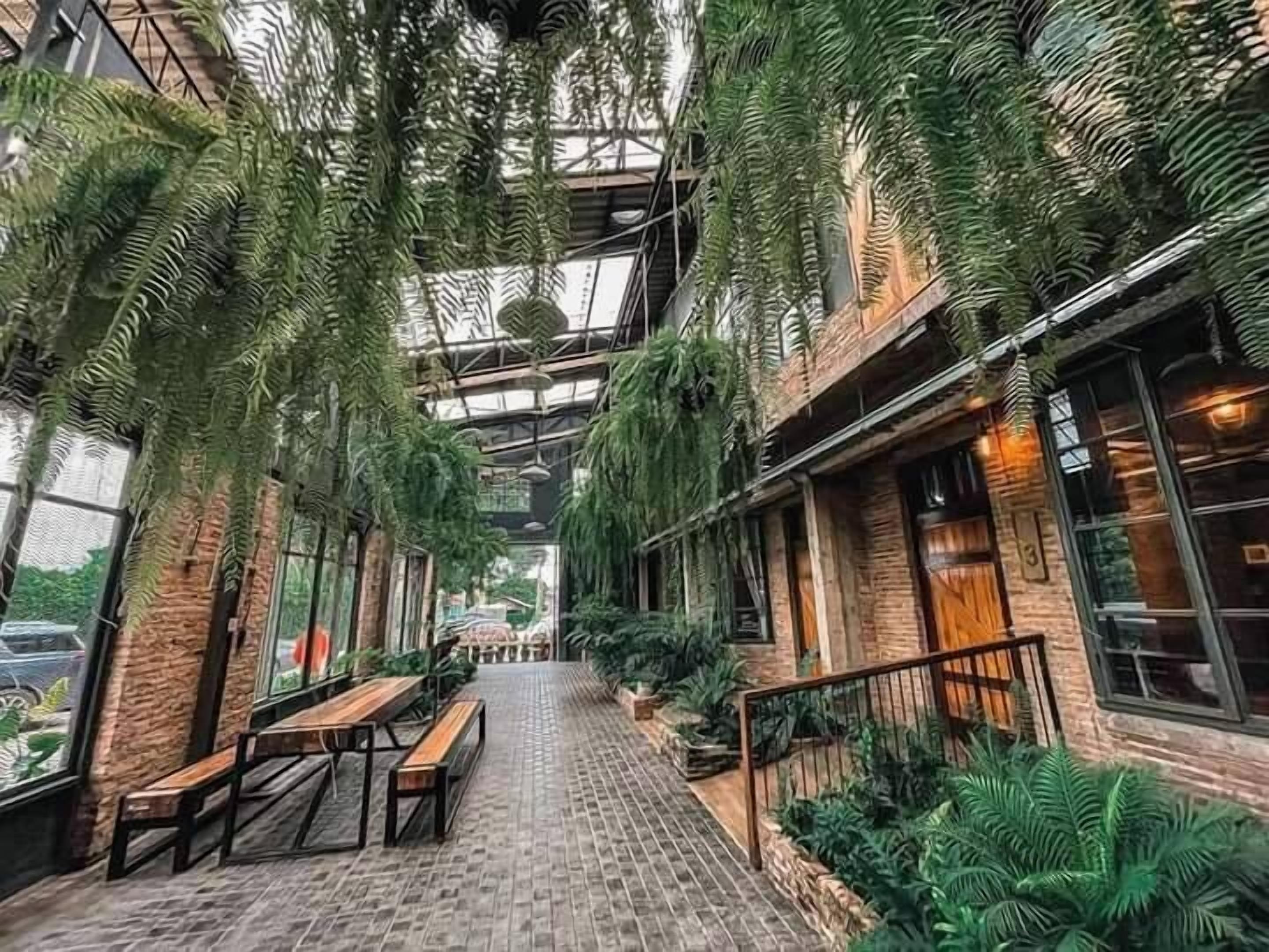 An indoor space with a brick floor, wooden benches, and hanging plants.
