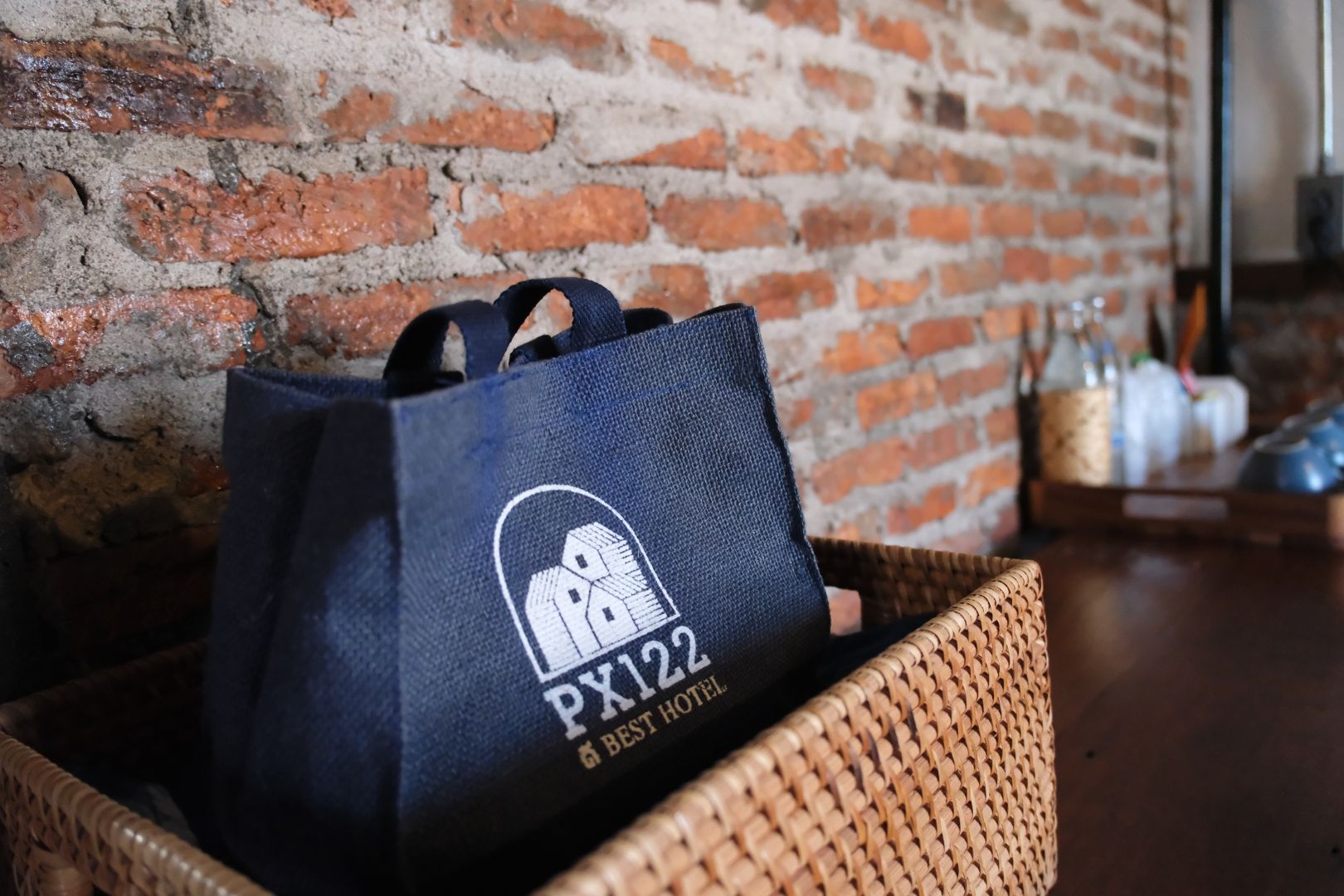 A dark blue hotel bag with the logo and name 'PX122' and the tagline 'BEST HOTEL' in a wicker basket.