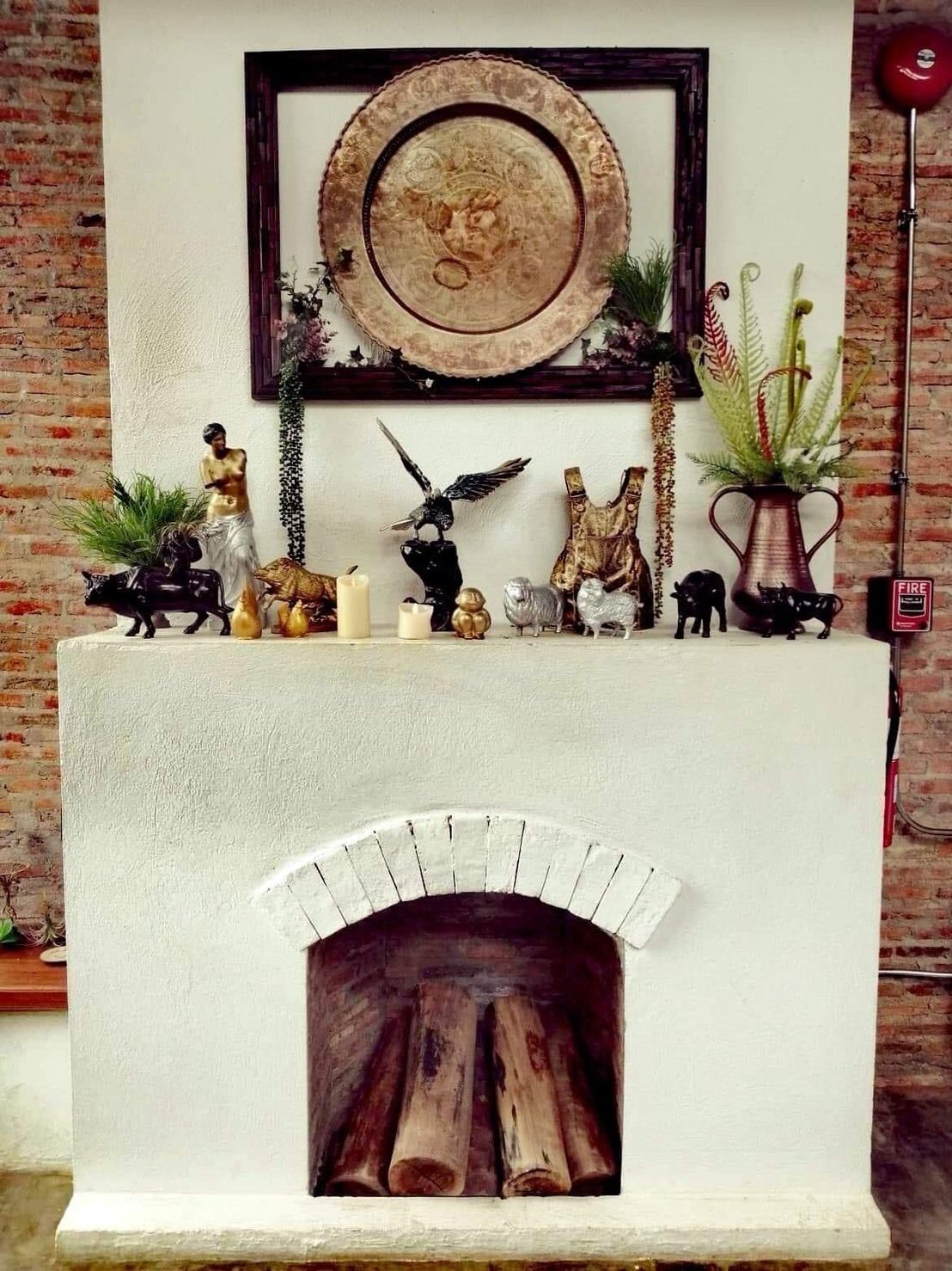 Une cheminée avec un manteau de style rustique, orné de diverses figurines, d’une œuvre d’art encadrée et d’une plante en pot.