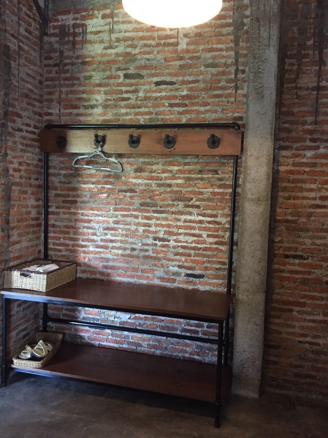 A rustic room with exposed brick walls, a wooden bench with a metal hanger, and a basket on the bench.