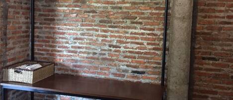 A rustic room with exposed brick walls, a wooden bench with a metal hanger, and a basket on the bench.