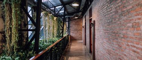 A corridor with brick walls, a wooden railing, and hanging greenery.
