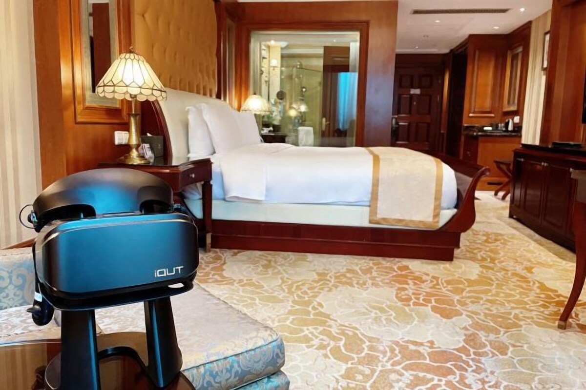 A hotel room with a bed, a desk, a lamp, and a suitcase.