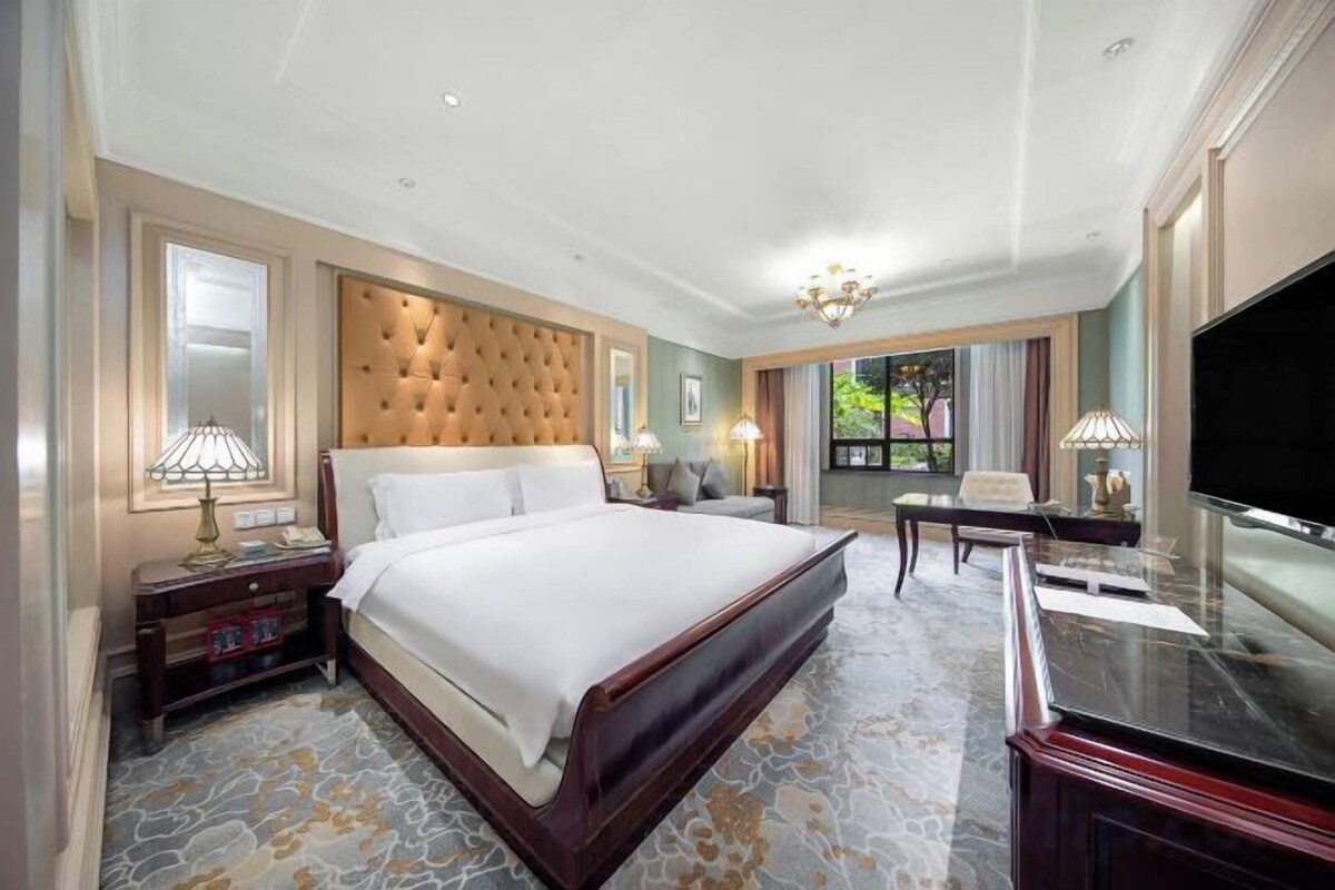 A hotel room with a large bed, a television, a desk, and a view of the outdoors.