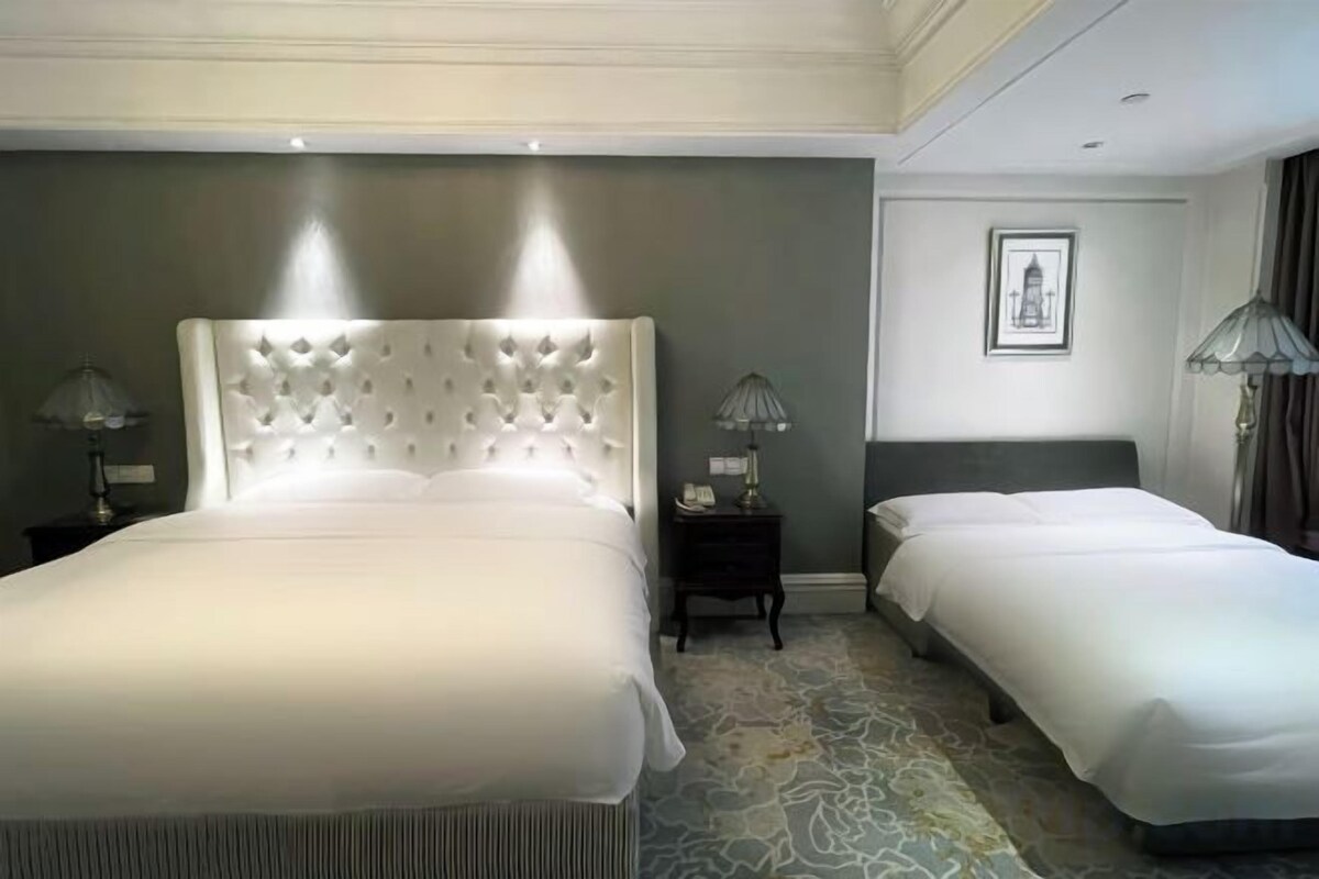 A hotel room with a large bed, two bedside tables, a nightstand, a framed picture on the wall, and a patterned carpet.