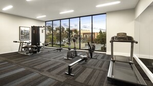 A gym with cardio equipment, weight machines, and a large window offering a city view. - Quest Maribyrnong (Maribyrnong)