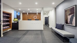 A modern reception area with a wooden reception desk, a bench, and a wall-mounted artwork. - Quest Maribyrnong (Maribyrnong)
