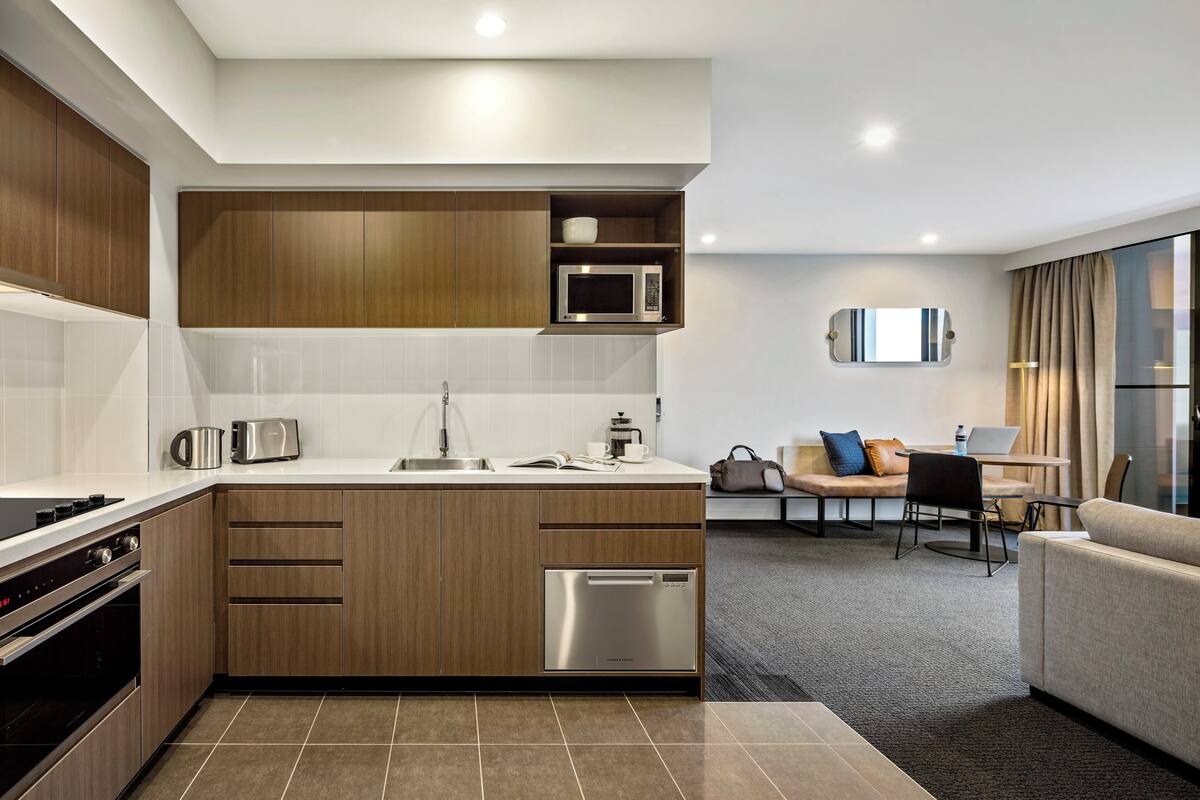A modern kitchen with built-in appliances, a dining area with a sofa and table, and a view of the city through large windows.